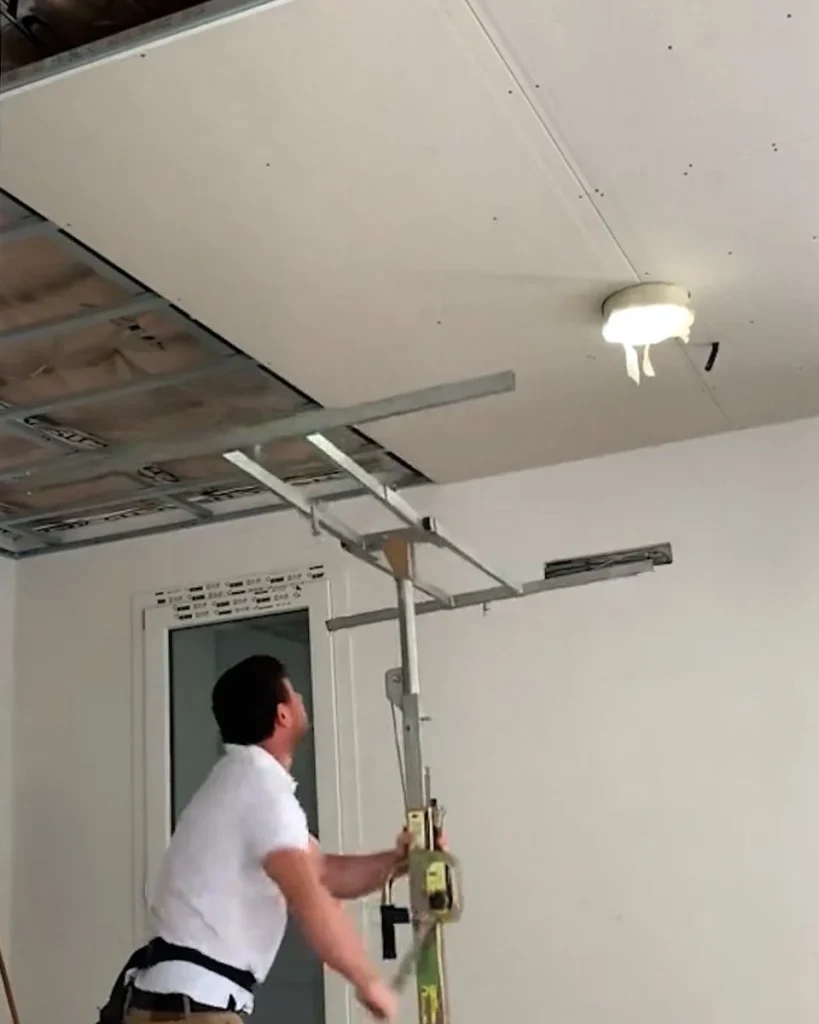 Contractor installing drywall ceiling panels with a drywall lift during residential interior construction and home renovation work.