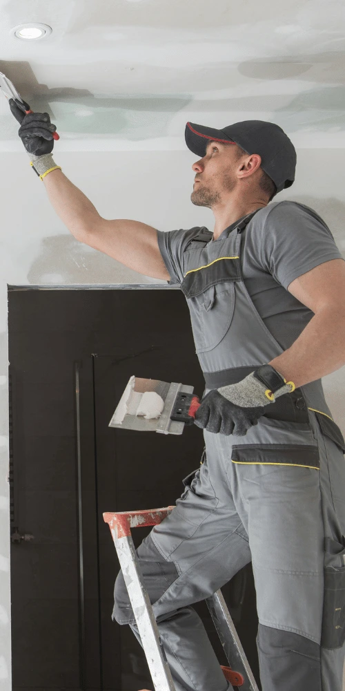 Drywall contractor applying joint compound to a ceiling while standing on a ladder during an interior drywall finishing and repair project.