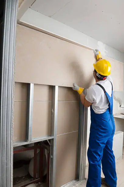 Drywall installer securing gypsum wall panels to metal stud framing during commercial interior construction and renovation.