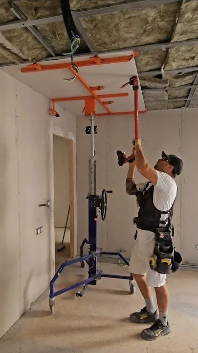 Professional drywall installer using a panel lift to install ceiling drywall sheets in a commercial interior construction project.