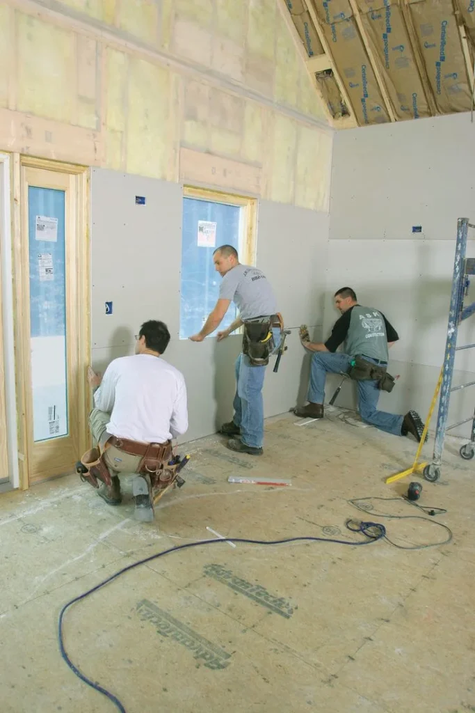 Professional drywall installers fitting wall panels around windows during residential drywall installation and interior construction.