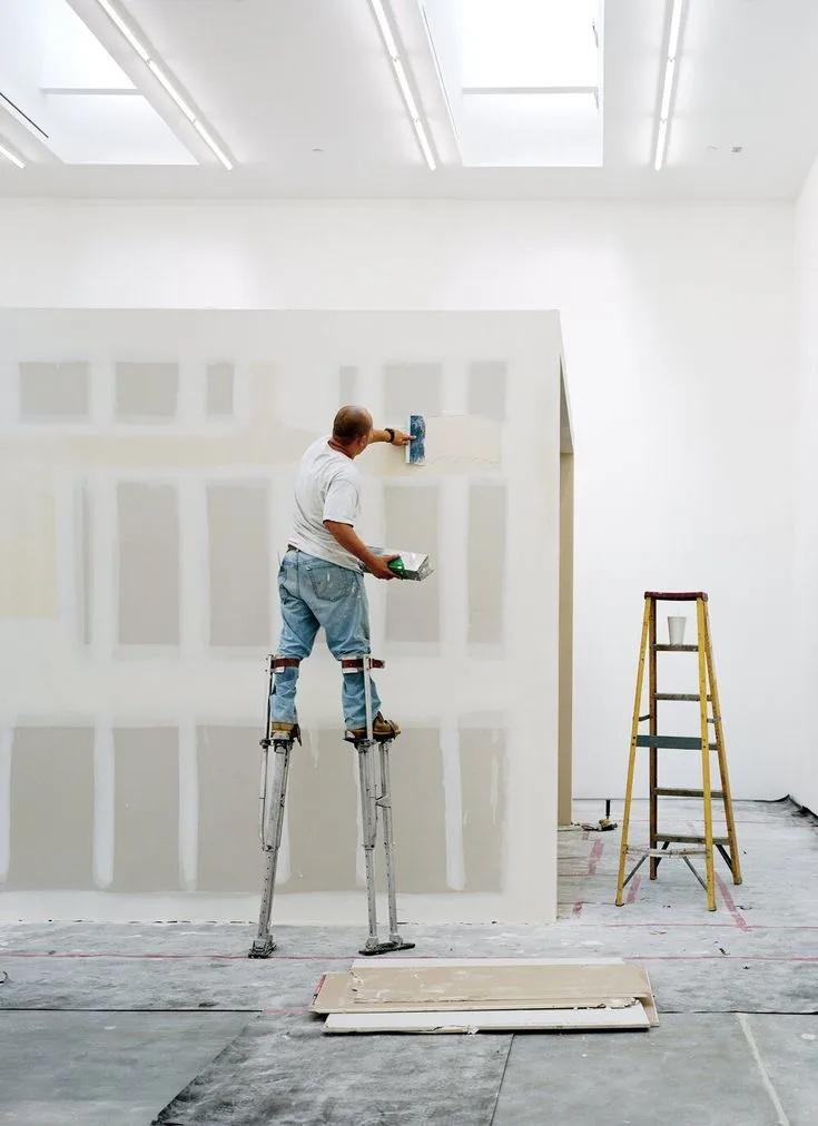 Drywall finisher applying joint compound to interior walls during commercial drywall finishing and surface preparation.