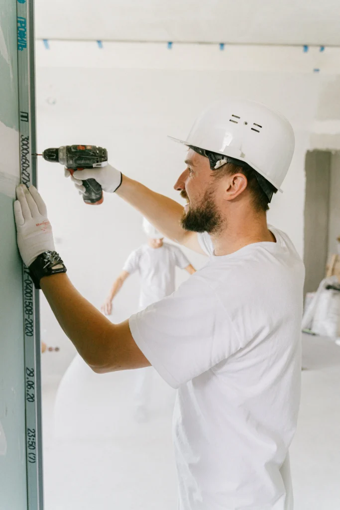 Contractor using a power drill to install drywall framing inside a residential interior.